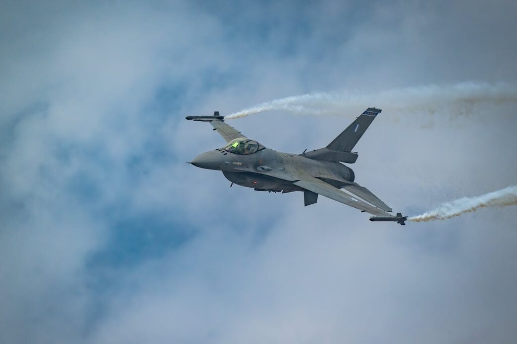 A fighter jet performing an aerial maneuver with vapor trails against a cloudy sky.